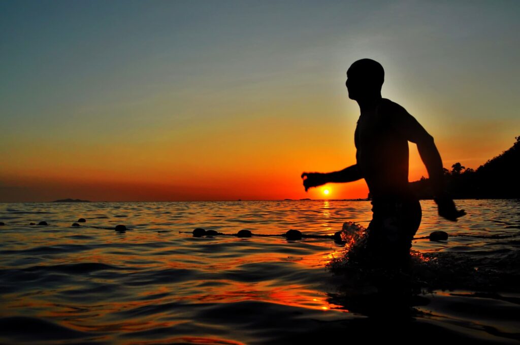 Swimmer running into the sea at sunset